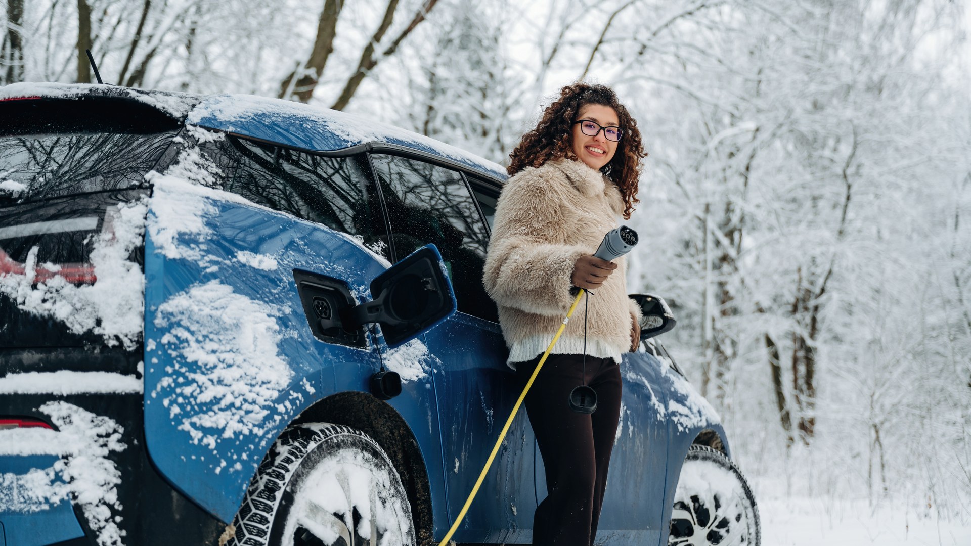 Frau lädt Elektroauto im verschneiten Winterwald – E-Auto Reichweite im Winter