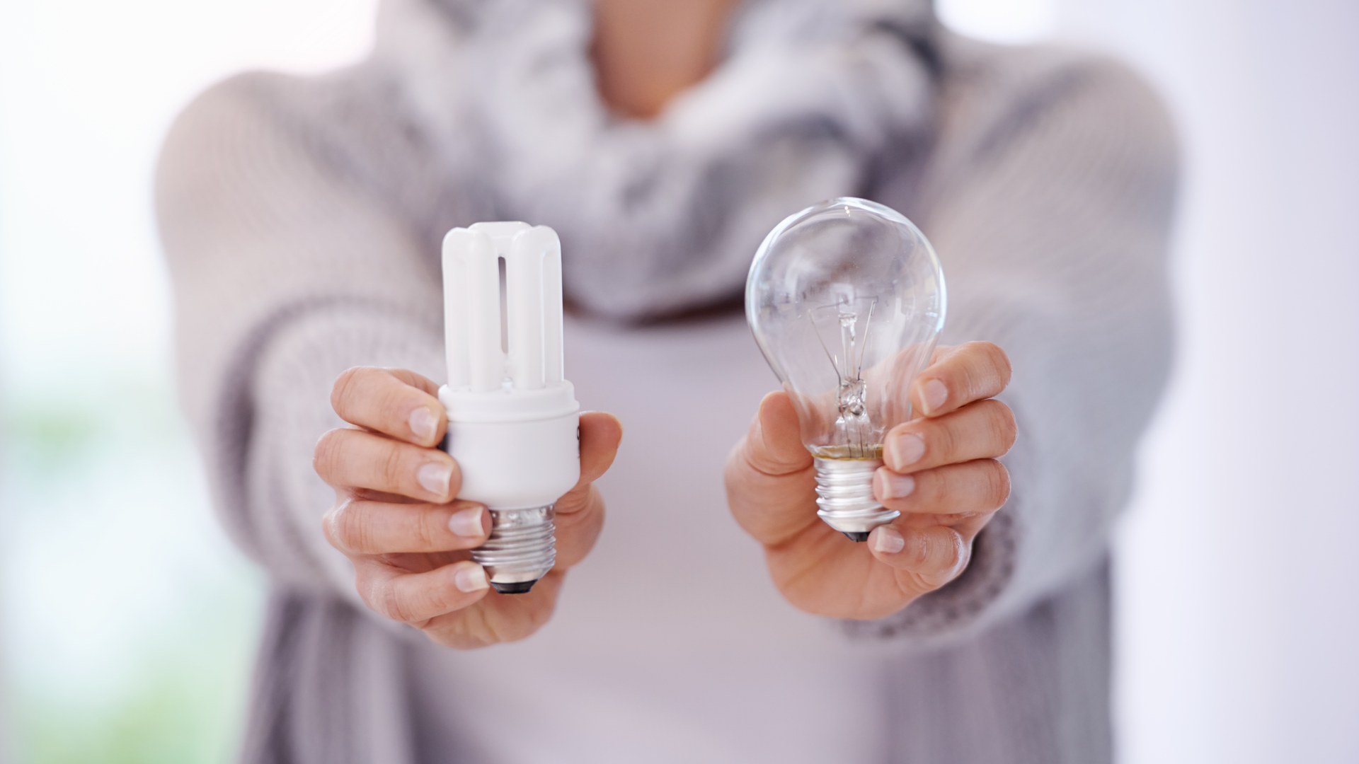 Frau hält LED-Energiesparlampe und alte Glühbirne im Vergleich