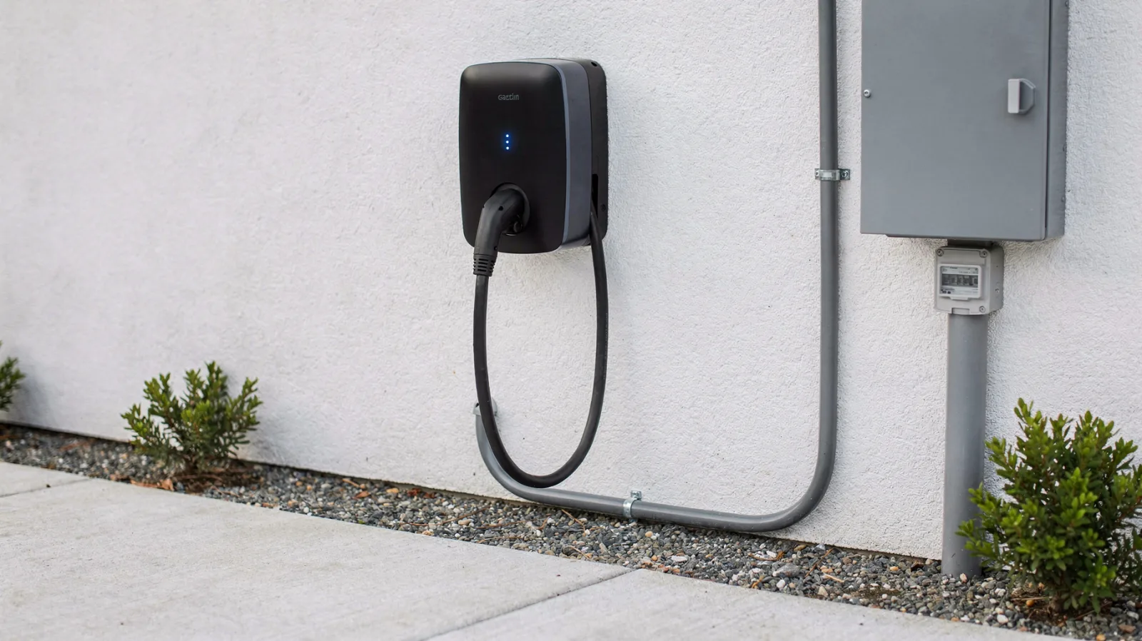 Wallbox an einer Hauswand mit Ladekabel und Sicherungskasten im Hintergrund